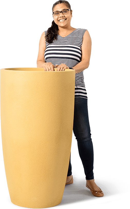 a happy woman standing with her hands on a tall planter